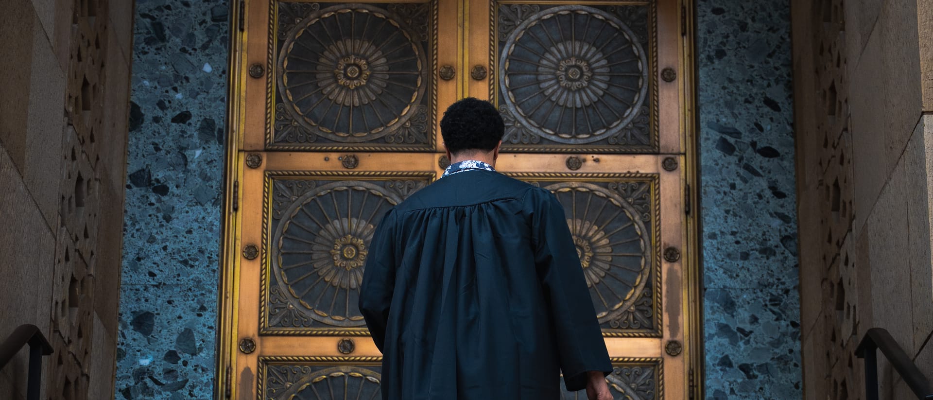 Graduate ascending stone steps toward grand golden doors in downtown Phoenix, Arizona