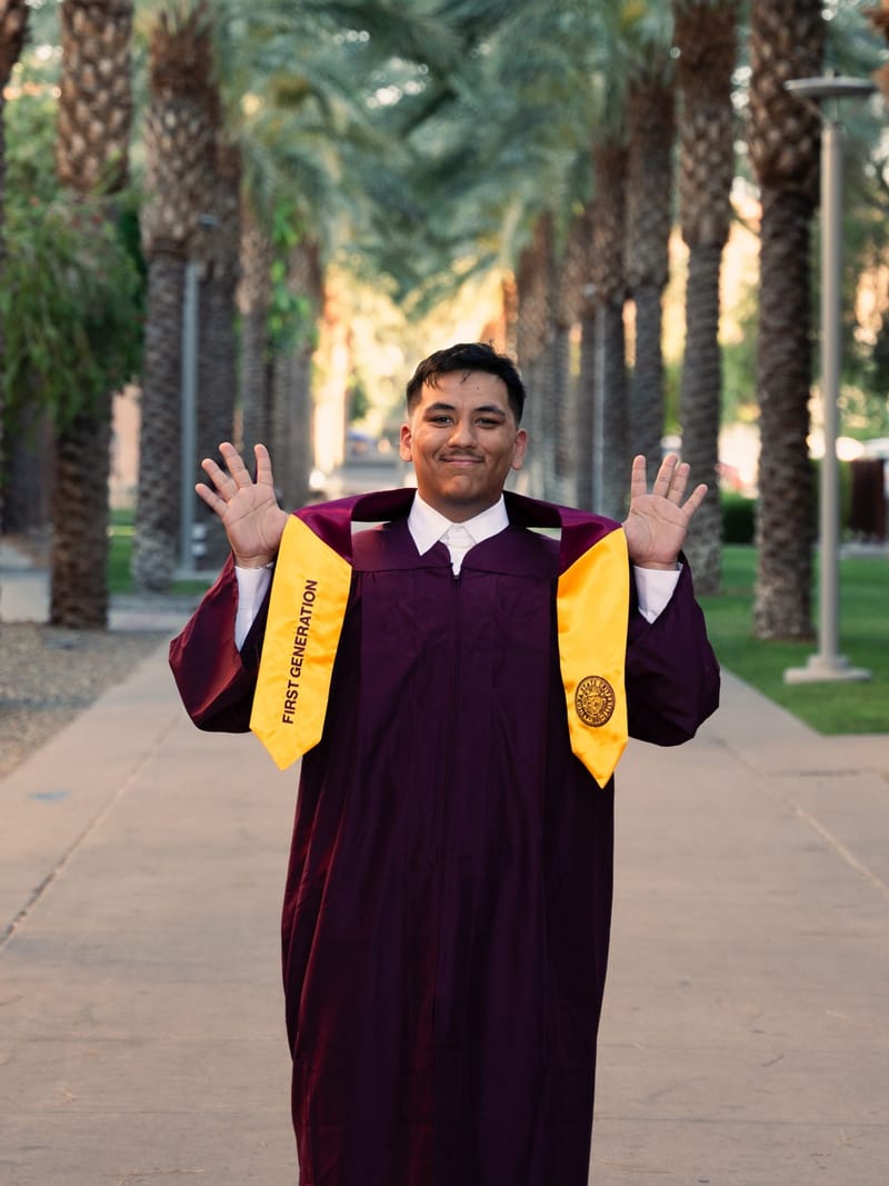 ASU graduate with arms out celebrating on Palm Walk, maroon gown, Tempe, Arizona