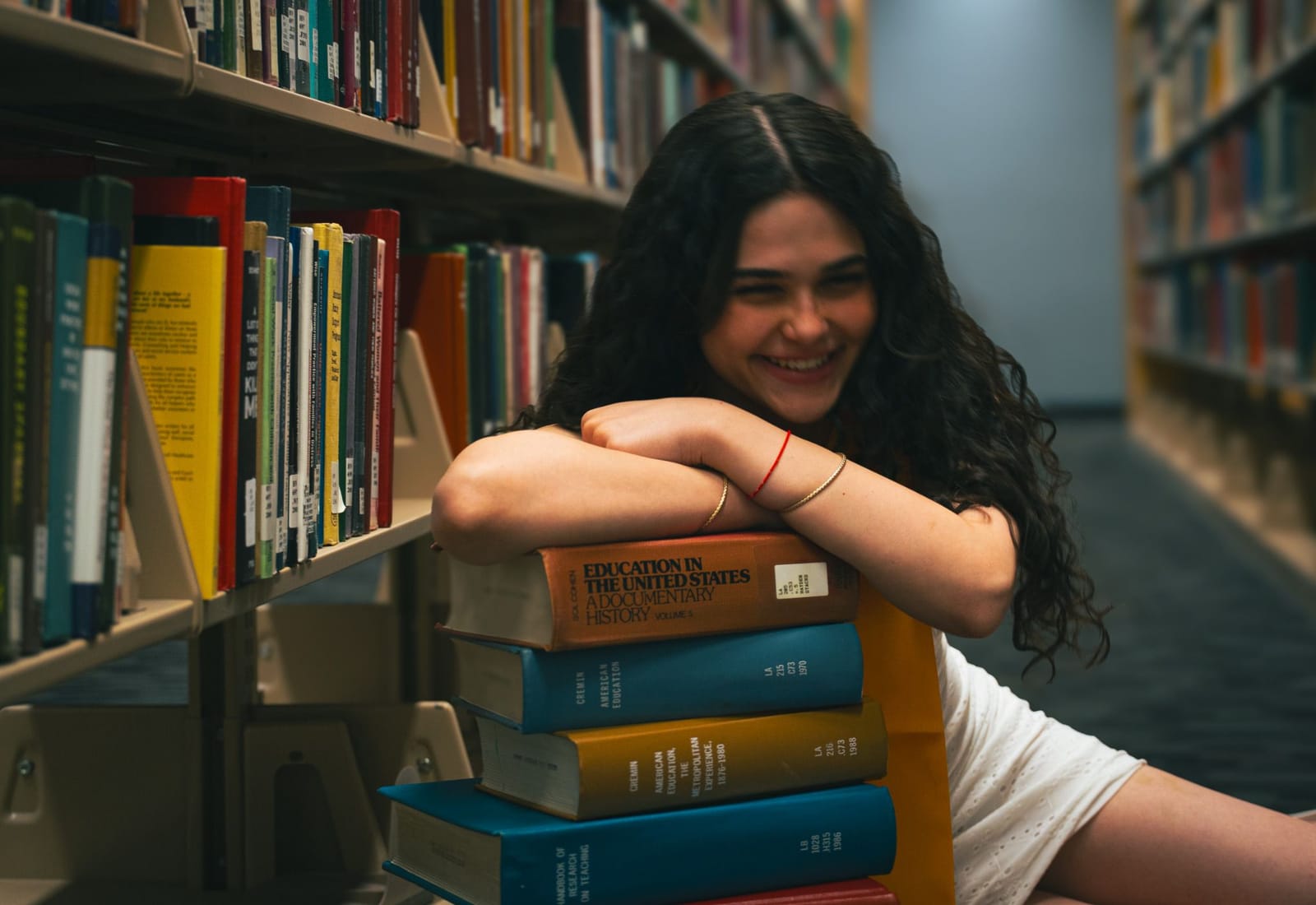 ASU graduate laughing behind a stack of books in the library, gold stole, Tempe, Arizona