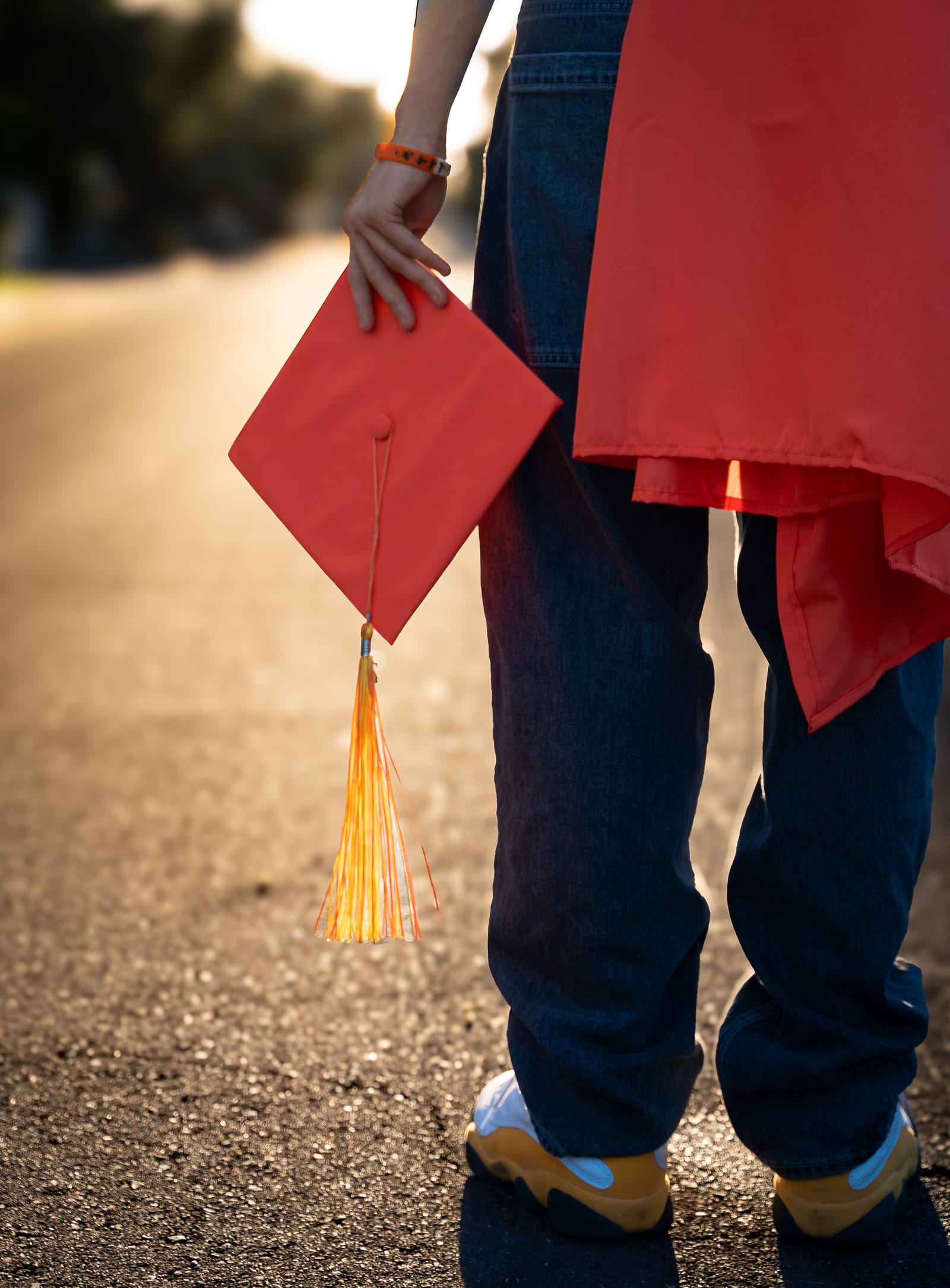 Graduate holding a red cap with tassel behind their back on a backlit street, Phoenix, Arizona