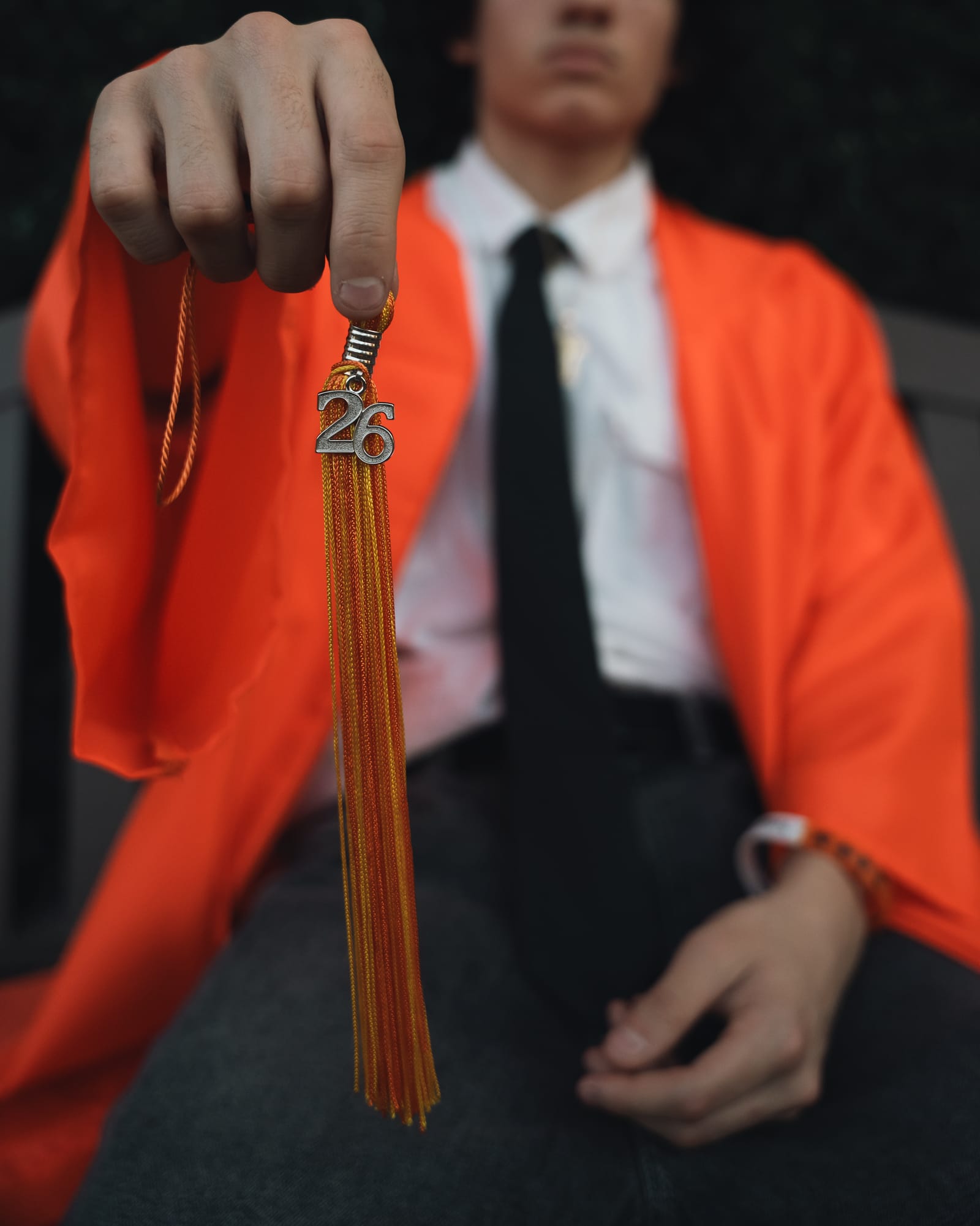 Close detail of a red graduation gown over a suit with tassel in hand at golden hour, Phoenix
