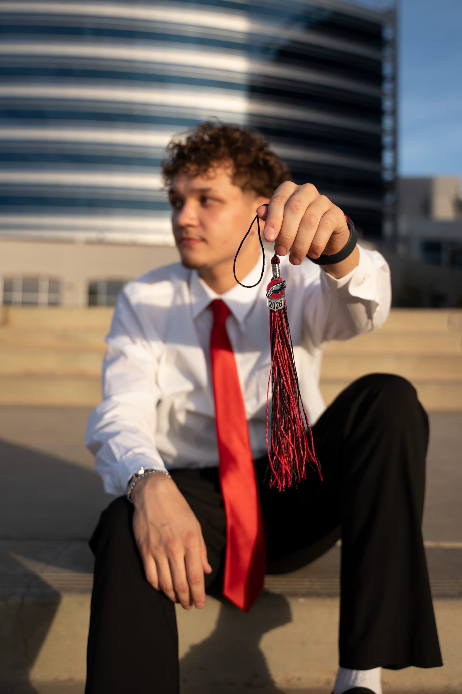 Senior in white shirt and red tie holding his graduation tassel, moody downtown Phoenix portrait