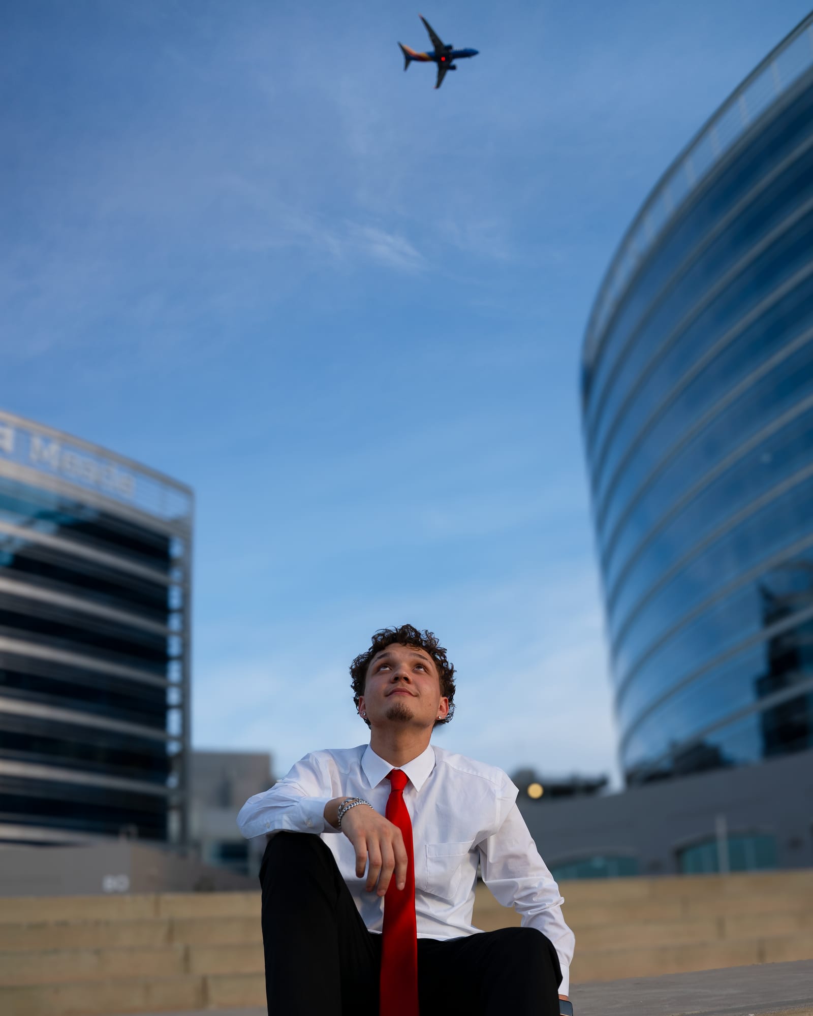 High school graduate standing before modern glass architecture at dusk in Tempe, Arizona