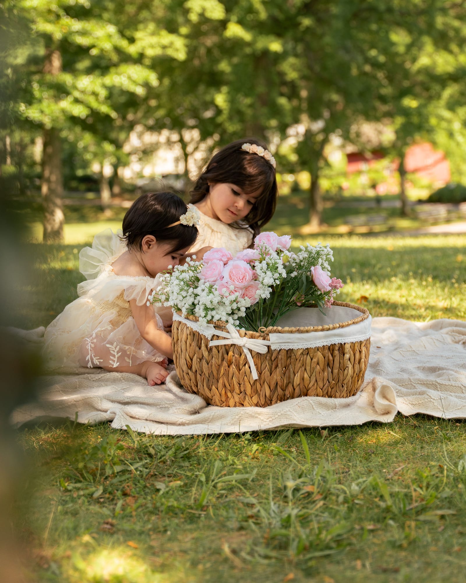 Two young sisters leaning over a woven basket of roses on a blanket under summer trees, Roslyn, New York