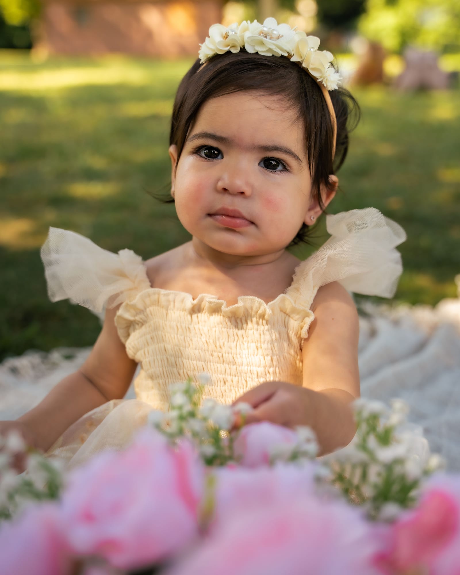 Portrait of a one year old in a cream tulle dress and flower crown beside pink roses, Roslyn, New York