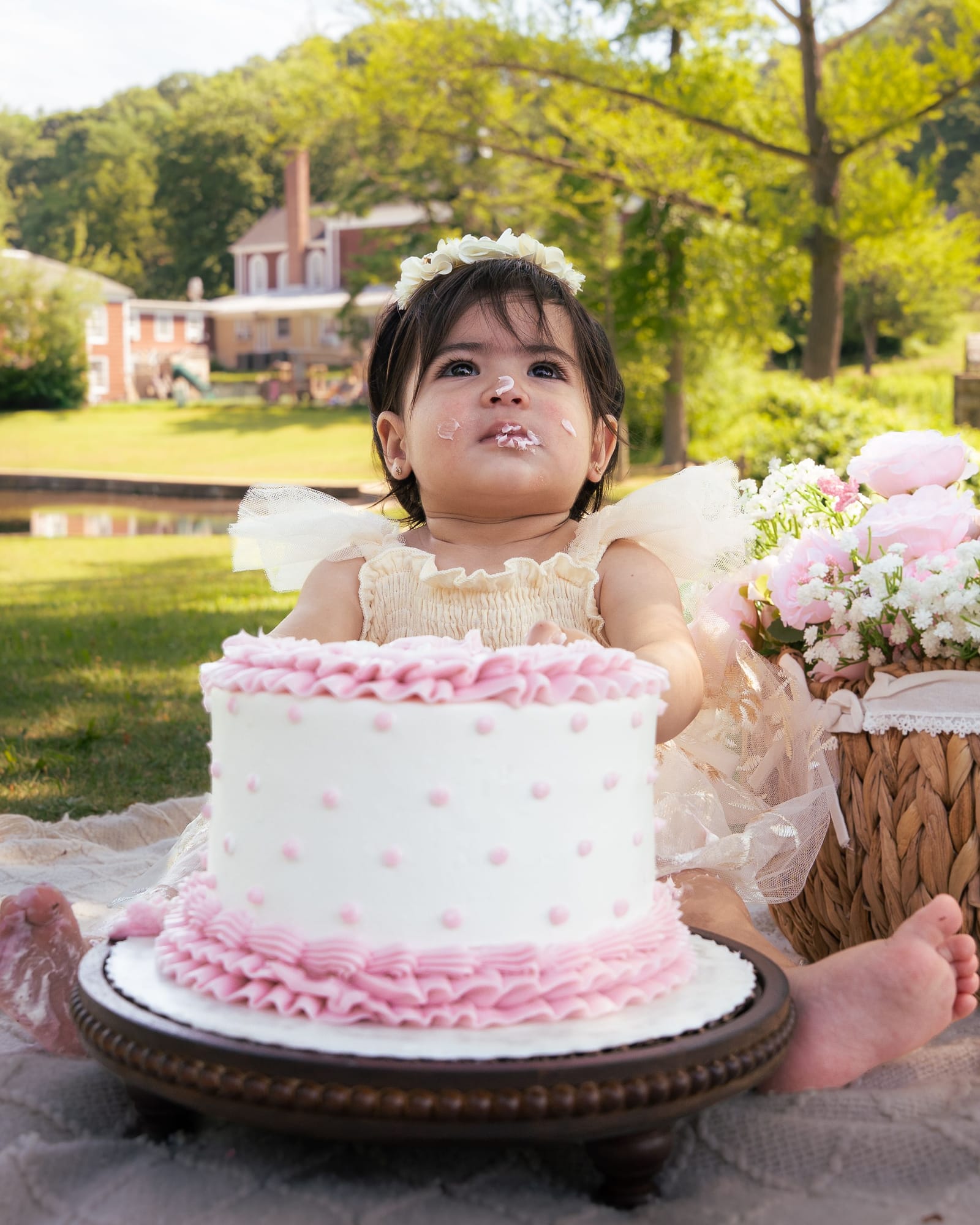 One year old with frosting on her face behind a pink ruffled smash cake in a park, Roslyn, New York