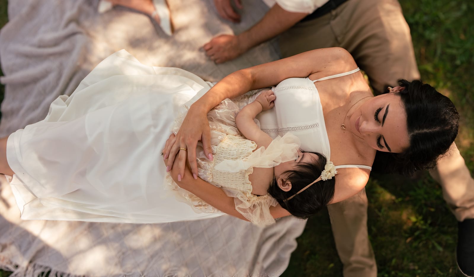 Overhead photo of a mother in a white dress cradling her baby on a picnic blanket, Roslyn, New York