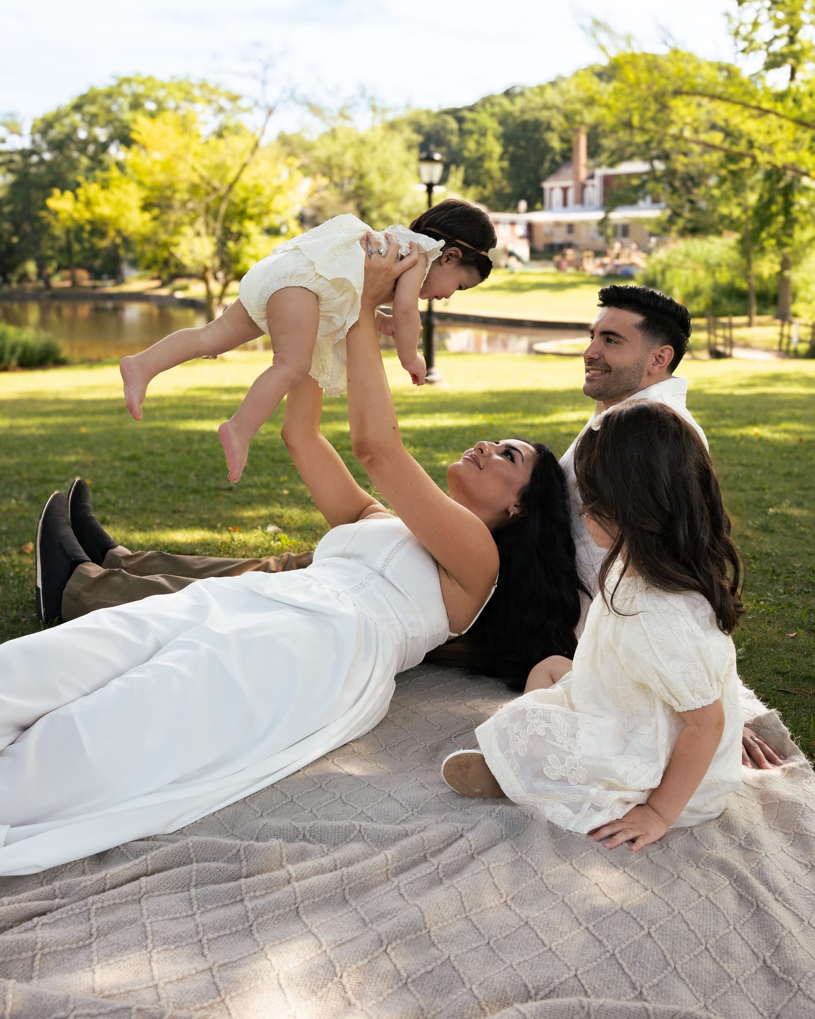 Mother lying on a picnic blanket lifting her baby overhead while father and sister watch, Roslyn, New York