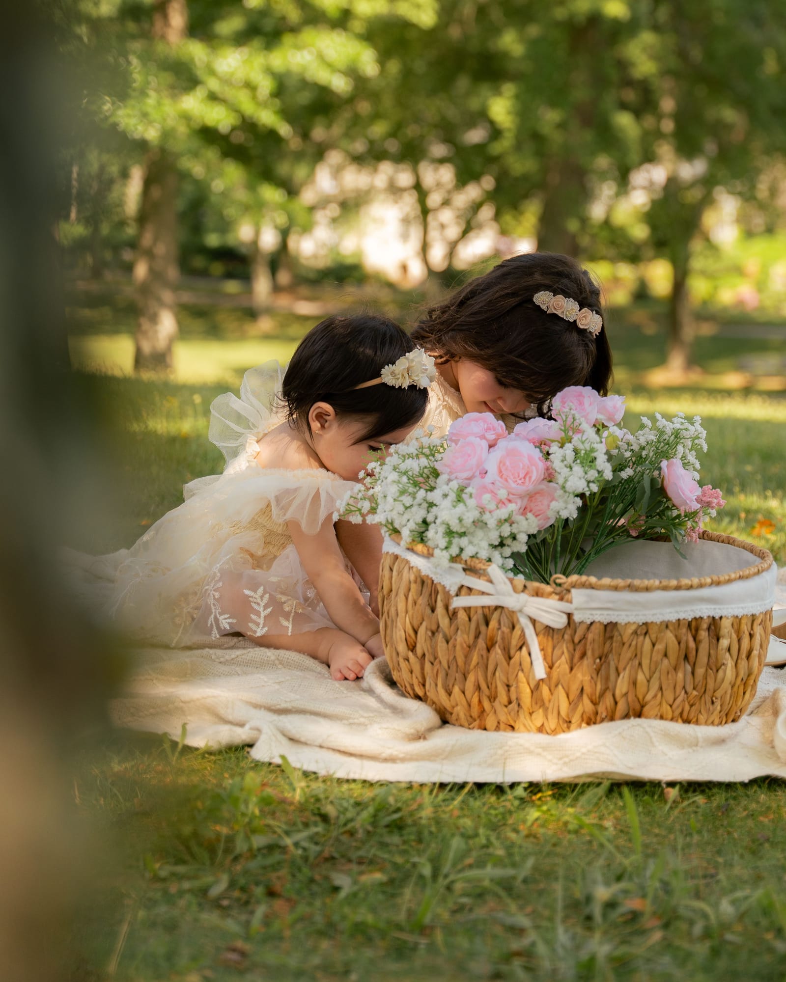 Baby and her older sister leaning in to smell pink roses in a basket, Roslyn, New York