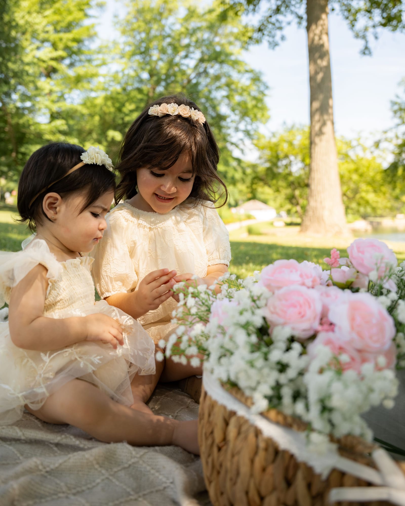 Two sisters in cream dresses and flower crowns beside a basket of pink roses, Roslyn, New York