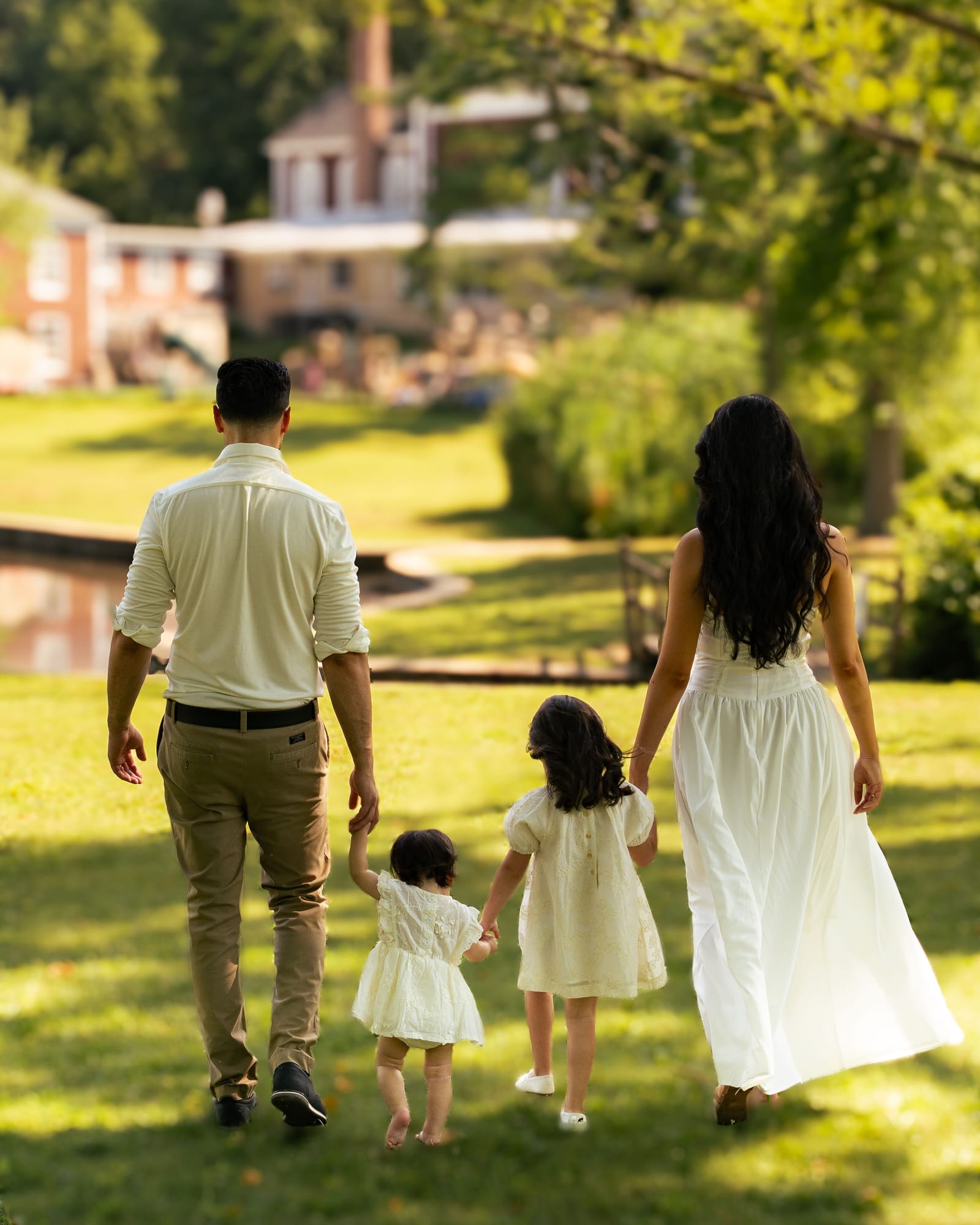 Family of four walking away hand in hand toward a pond and stone house, Roslyn, New York